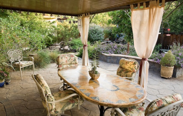 Table and chairs in garden room with privacy curtains, outdoor stone patio, California drought tolerant garden