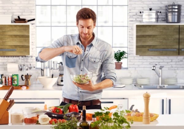 Handsome man cooking at home preparing salad in kitchen.