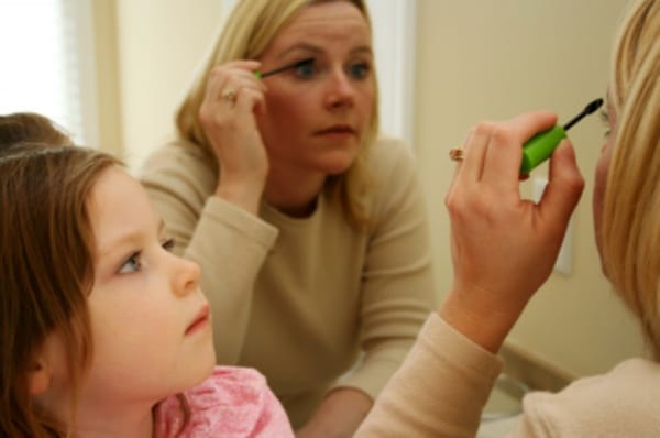 A girl watches her mother putting on makeup